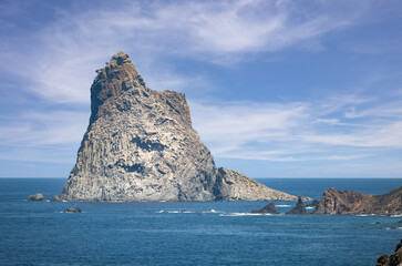 A telephoto shot of the most famous rock of Anaga on the northeast side of the Atlantic island of Tenerife. The air on this sunny day is very hazy. In the background is a fishing boat.