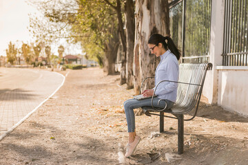Fototapeta premium Young woman working on her computer outdoors on a sunny afternoon sitting on a bench in the park