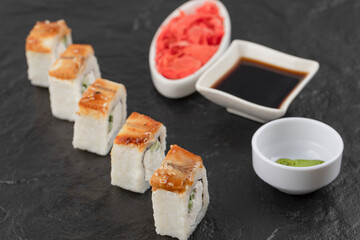 Dragon sushi rolls, wasabi, soy and pickled ginger on black surface