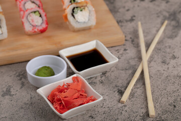 Wooden board of various sushi rolls with ginger and soy sauce on marble table