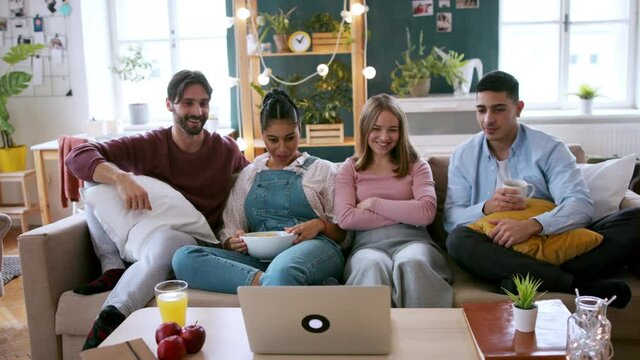 A group of flatmates sitting on sofa and watching movie, house sharing concept.