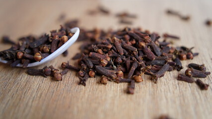 Indian dried clove spice on wooden table background. Dry aromatic flower buds, flowers in a spoon. Indian delicious spices
