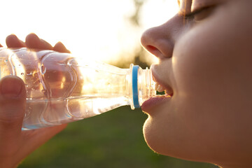 woman drinks water from a plastic bottle outdoors in summer close-up
