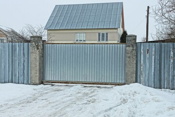 Fototapeta premium gray metal gate and part of a wall fence in white snow on a winter street