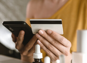 Close up of woman purchasing cosmetics online with smartphone and credit card.