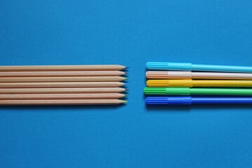 set of brown wooden pencils and colored plastic markers on blue table