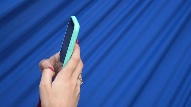 Close Up Of Young Woman Hand With Red Nails And Ring Typing Text Message On Cell Phone Chat On Blue Fabric Background. Concept Of Technology, Lifestyle.