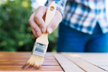 young woman painting wooden exotic wood table in the garden with a brush