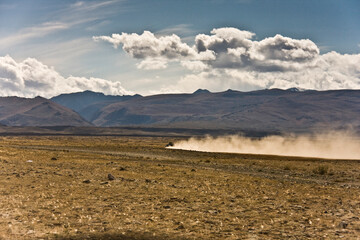 Autotourism, off-road in the mountains. The car drives through the valley between the mountains, leaving a dusty trail