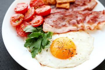 Fototapeta na wymiar English breakfast - fried eggs, herbs, tomatoes, bacon and crackers