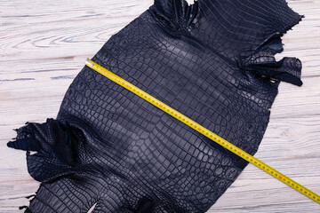Natural dark-blue dyed alligator leather with ruler lies on a wooden table