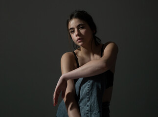 Portrait of a beautiful stylish girl in black bra and denim jeans sitting and looking at camera.