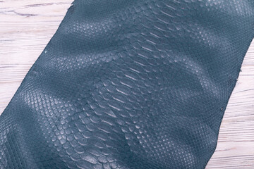 Blue-gray dyed genuine natural python skin folded on a wooden table.