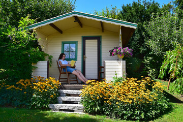 Fototapeta na wymiar A teenage girl sitting in a chair on the porch of a garden shed, reading a book.