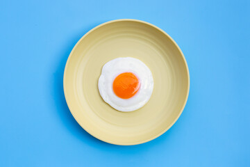 Fried egg in yellow dish on blue background.