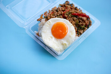 Rice topped with stir-fried pork with holy basil and fried egg in plastic food container