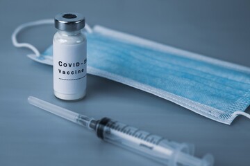 Vaccine ampoule with COVID-19 inscription, injection syringe and medical protective mask on a gray background. Coronavirus vaccination concept