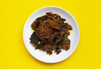 Stir fried catfish with curry paste on yellow background.