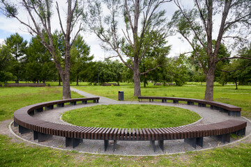 Round wooden bench in the park, standing under the trees. Modern fashionable design round circular...