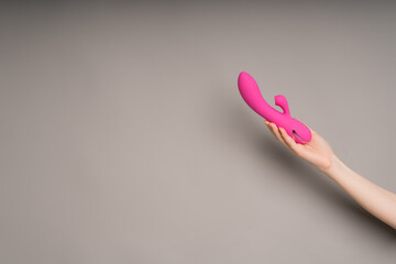 Bright pink vibrator in a female hand on an orange background. Massager for masturbation. Dildo, toys for adults