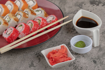 Red plate of various sushi rolls with wasabi and pickled ginger on marble table