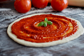 Raw pizza dough with tomato sauce and basil leaves. Selective focus