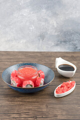 Bowl of sushi rolls and red caviar on wooden table with soy and ginger