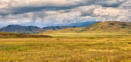 Amazing landscape of yellow steppe and mountains. Storm clouds and rain in the mountains.