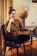 Pregnant woman sitting at home and using laptop.