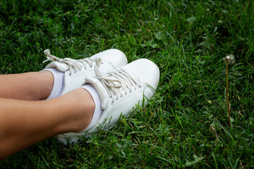 Female feet in white sneakers on green grass. Activity and relaxation during the warm season....