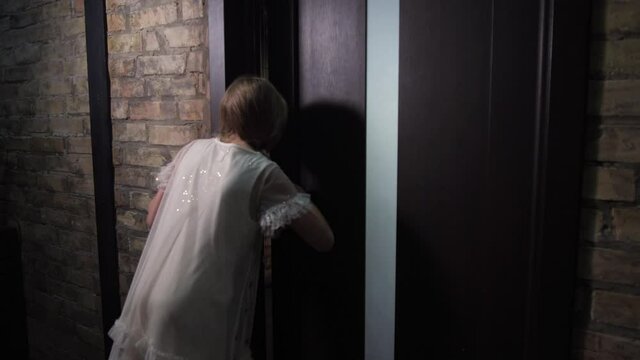 Back view of curious child opening door and watching through crack at young dancers practicing in dance hall. Girl peeping at dancer's lesson reflected in mirrored wall, dreaming to become ballerina