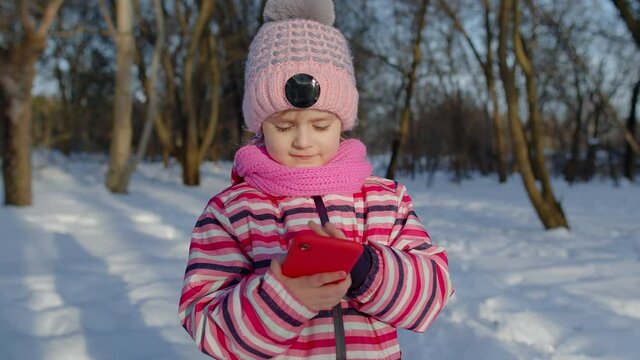 Children kid tourist blogger browsing on mobile phone, publishing new photo picture post on social media, thumbs up. Child girl chatting with friends and family, distance communication in winter park