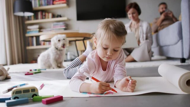 Girl at home drawing a picture while her parents are working. Homeoffice concept.