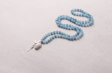 Rosary mala 108 beads from natural stones aquamarine lie on light modern background. Author's jewelry from natural stones, Buddhism, matra, prayer, rosary from stones for prayer, beauty. Long beads