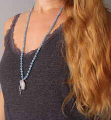 Rosary mala 108 beads from natural stones Aquamarine are worn on a girl in a grey shirt. Author's jewelry from natural stones, Buddhism, matra, prayer, rosary from stones for prayer and beauty
