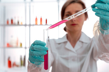 The laboratory assistant holding test tube, pipetting liquid. Focus on hands.