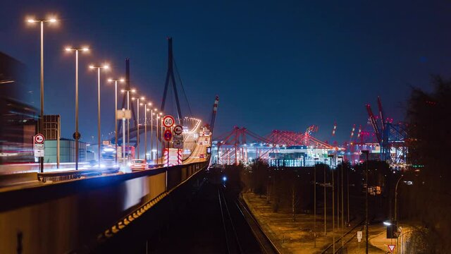 Timelapse of the Koehlbrand bridge with cars and trucks on the ramp Eurokai and Burchardkai Terminal in the distance at night. Clear sky above Hamburg Harbor during night.