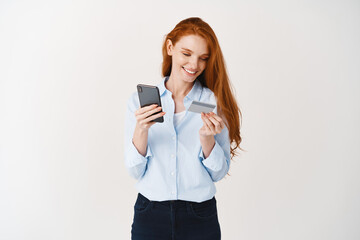 Young attractive woman shopping online with smartphone and plastic credit card, making purchase in internet, white background