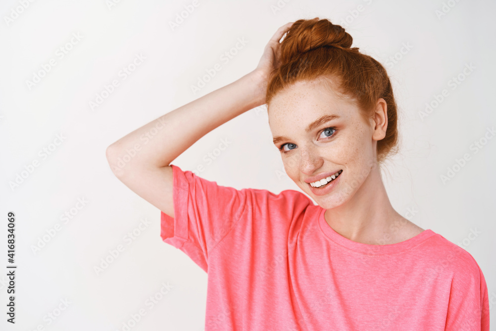 Wall mural Beauty and skincare. Young woman with red hair combed in messy bun smiling cute at camera, showing healthy glowing skin without acne and blemishes, white background