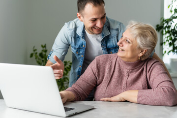 Adult mother and son consider new software on laptop sitting at table