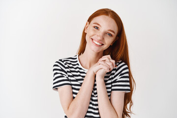 Lovely redhead girl admire something, clasp hands together and smiling thankful, standing delighted against white background