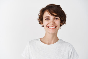 Portrait of beautiful natural girl without makeup, smiling happy at camera, standing in t-shirt against white background