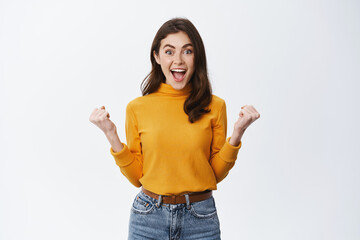 Cheerful beautiful woman celebrating, looking with disbelief and excitement as winning prize,...