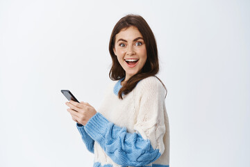 Portrait of cheerful brunette woman turn head at camera after reading news on mobile phone screen,...