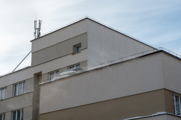 View of the facade of a modern concrete building or office center. The roofs of the buildings are covered with snow and ice after a big snowfall. Modern 5g antenna on the roof of the business center