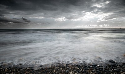 Obraz premium Seawaves splashing to the coast with stones against stormy dramatic cloudy sky. Wintertime, Limassol cyprus