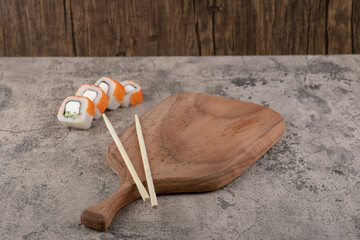 Traditional sushi rolls and chopsticks around wooden cutting board