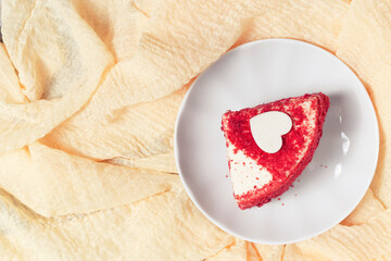 A piece of red cake on a white plate, background from a texture of bright yellow viscose fabric, top view.