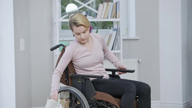 Young female paralyzed figure skater putting away ice skates and rolling wheelchair leaving. Side view of depressed paraplegic Caucasian woman having sport trauma after competition. Disability concept