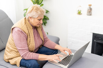 Serious mature older adult woman watching training webinar on laptop working from home or in office. 60s middle aged businesswoman taking notes while using computer technology